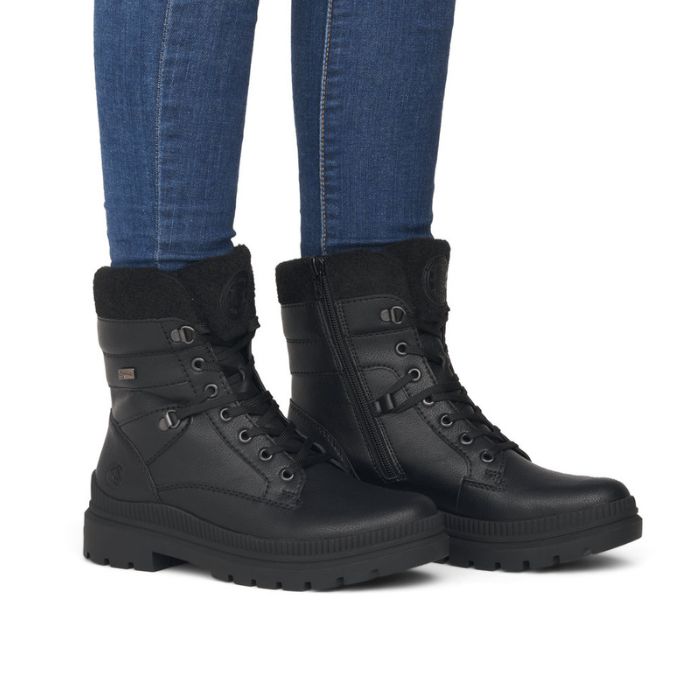 Legs in jeans wearing black leather combat boot with lace closure.