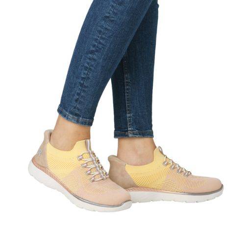 Model wearing Women's Rieker M5066 Slip-On Sneaker in peach-yellow, styled with jeans for a casual, sporty summer look.