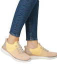 Model wearing Women's Rieker M5066 Slip-On Sneaker in peach-yellow, styled with jeans for a casual, sporty summer look.
