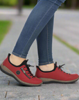 Red casual shoes worn with blue jeans on a blurred outdoor background.