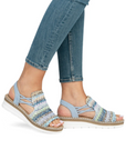 Model wearing pastel blue Women's Rieker V1241 Backstrap Sandals with jeans, showcasing comfort fit, colorful knit design, and flexible sole.