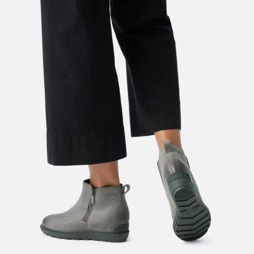 Model walking in grey Sorel Evie Zip II Wedge Boots paired with black pants, showing durable sole and stylish ankle boot silhouette.