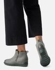 Model walking in grey Sorel Evie Zip II Wedge Boots paired with black pants, showing durable sole and stylish ankle boot silhouette.