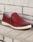 Red Josef Seibel Caren 22 leather slip-on sneaker for women displayed on a rustic white bench, combining comfort and casual elegance.