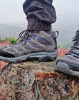 Women's Merrell Moab 3 Mid WP Boots in grey worn outdoors on a tree stump, showcasing waterproof hiking performance in rugged terrain.