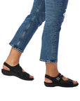 Girl in jeans wearing black backstrap sandals with silver accents.