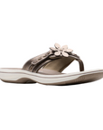 Bronze thong sandal with white midsole, bronze footbed with white designs including Clarks Cloudsteppers logo, fabric toe post, and adjustable bronze strap with bronze flower. Bronze outsole with rocker bottom design.