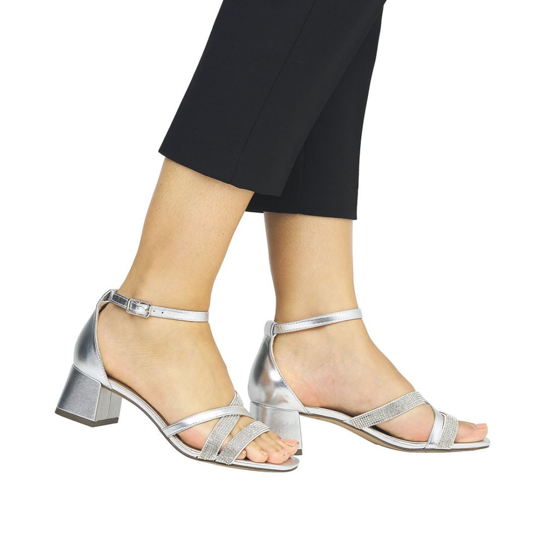 Model wearing silver Remonte D1L51 sling-back heels with ankle strap and glitter accents, ideal for formal or evening wear.