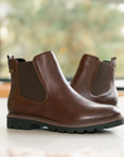 Pair of brown leather Chelsea boots on a light surface with a blurred background.