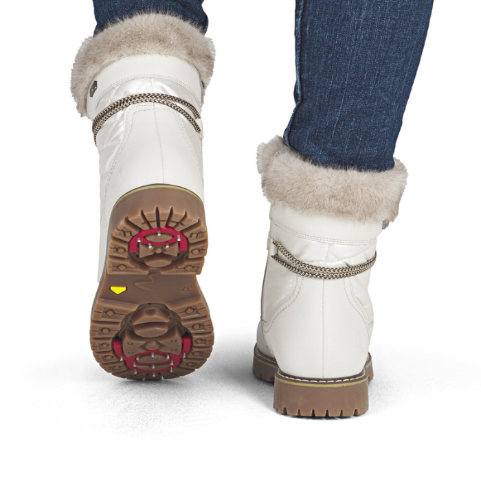 White winter boots with fur trim worn by a person with blue jeans.