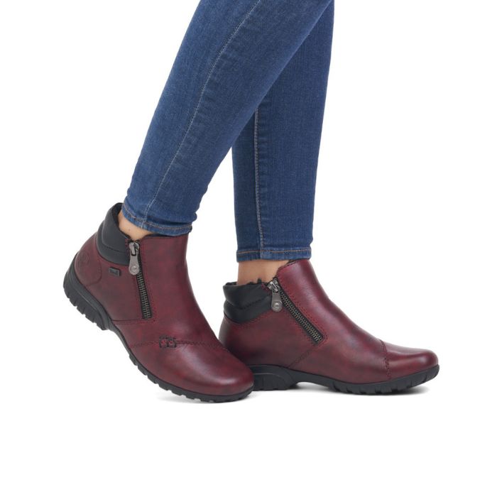 Legs in jeans wearing red ankle boot with black outsole and outside zipper closure.
