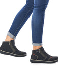 Black ankle boot with grey stitching details, few small red square designs and a front side zipper