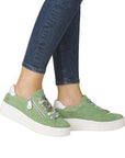 Model wearing green lace-up platform sneakers with colorful laces and white heel, paired with denim jeans.