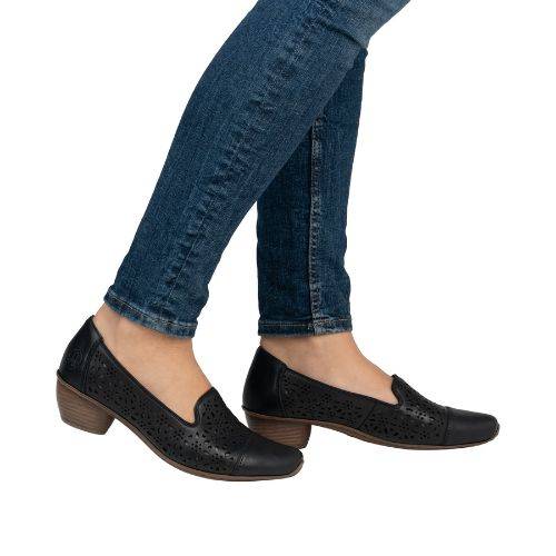 Model wearing heeled black perforated leather shoes with jeans.