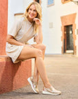 Woman sitting outdoors in a dress wearing Women's Rieker 48761 Slip-On Shoe, combining comfort and fashion with floral wedge design.