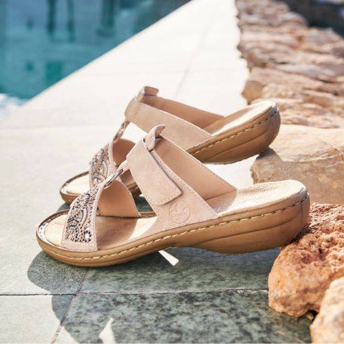 Beige Women's Rieker 608K2 Slide Sandals placed poolside, showcasing their stylish beaded design and summer-ready comfort.