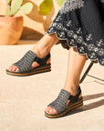 Model sitting outside wearing black and white woven Backstrap Sandals styled with a black patterned dress.