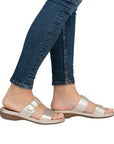 Legs of women in blue jeans wearing Rieker gold two strap slide sandals.