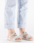Grey sandals with floral pattern worn with light blue jeans.