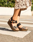 Model wearing black and leopard faux cork platform wedge sandals crossing street in spotted pants.