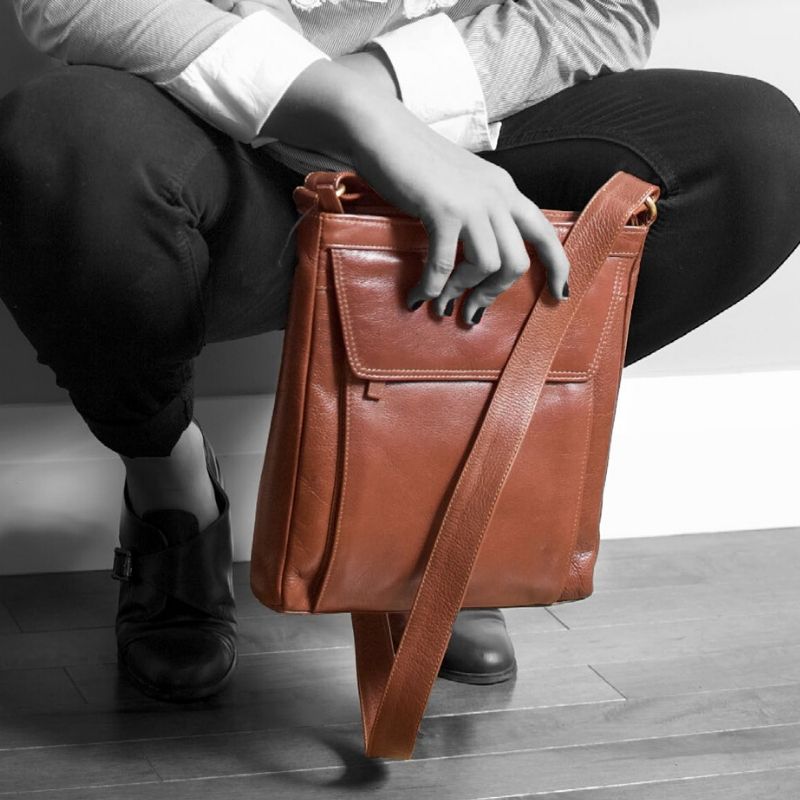 Greyscale photo of a woman crouching holding a brown Derek Alexander bag, which is in colour.