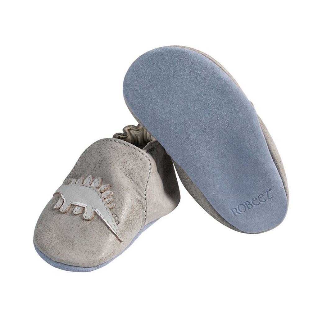 Left shoe shows Grey leather pull on kids shoe with dinosaurs, and right shoe tilted up to show soft blue bottom
