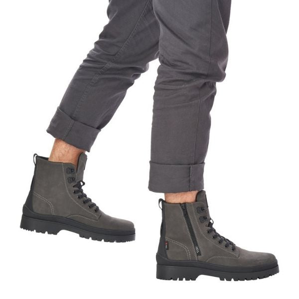 Man in grey pants wearing grey combat style winter boots with lace closure and outside zipper.