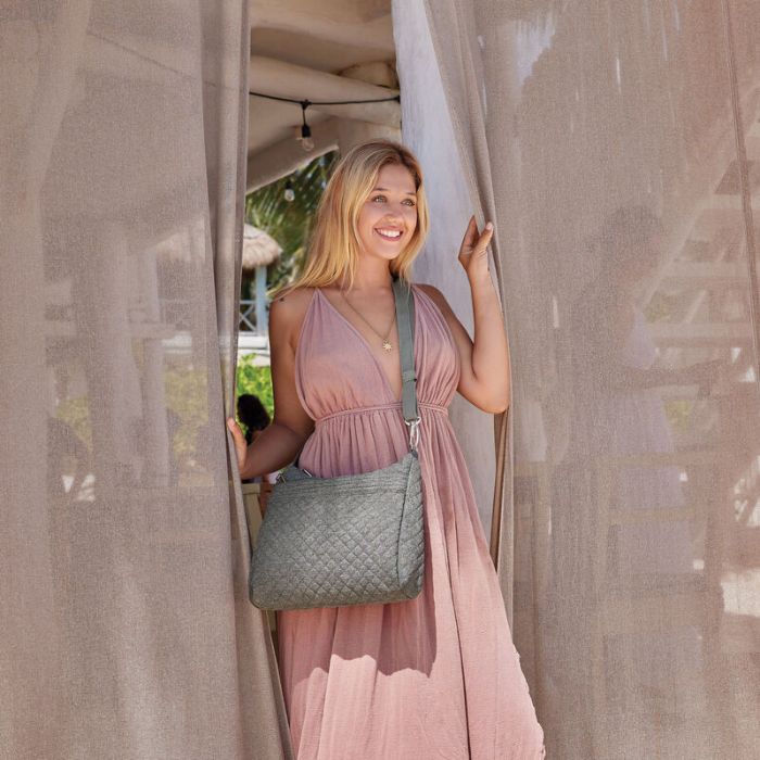 Women in a pink dress is wearing a grey quilted Travelon crossbody bag.
