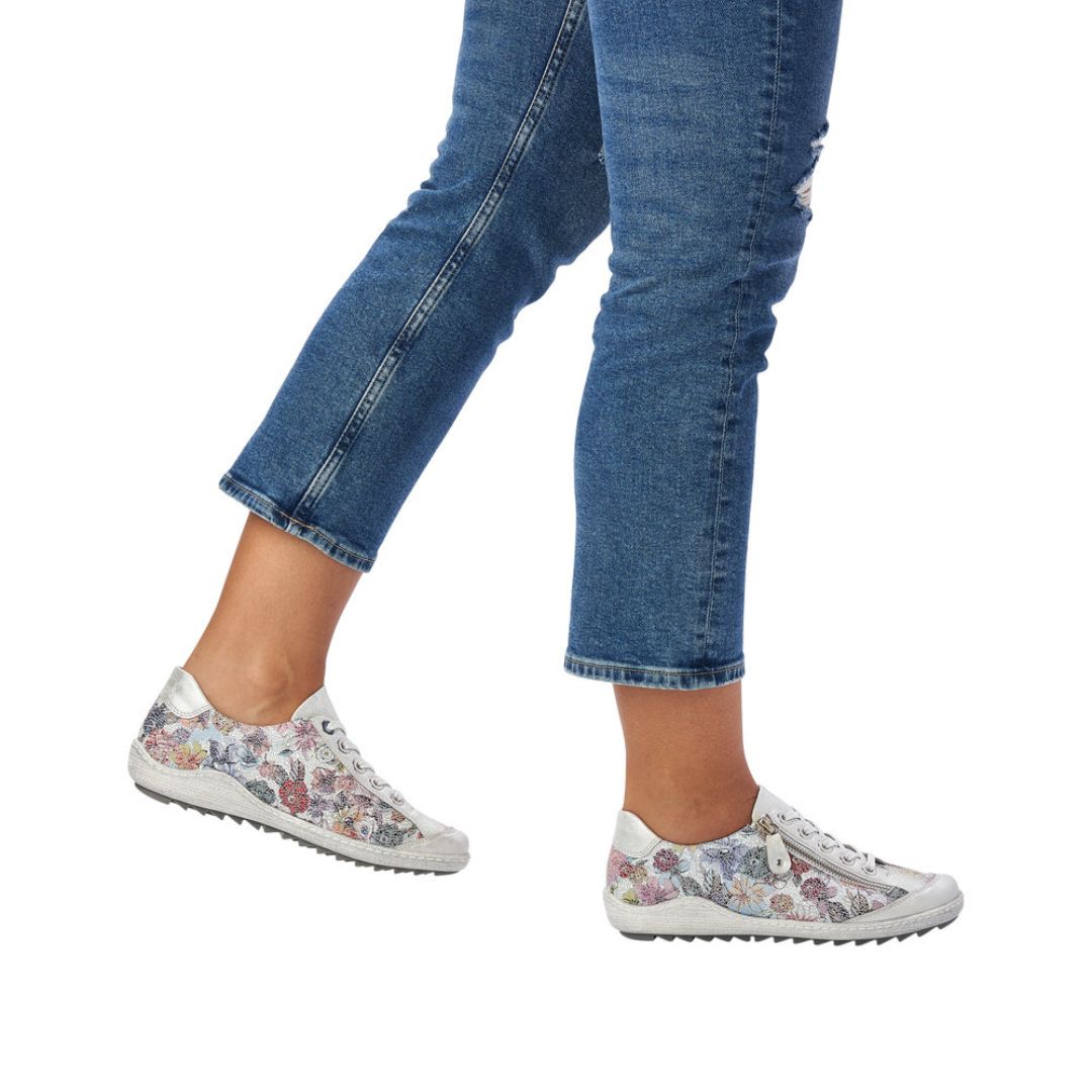 Legs in jeans wearing blue floral lace up shoe with zipper side closure and grey midsole.