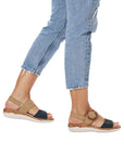 Model wearing Rieker R6853 Backstrap Sandal in tan and black, showcasing stylish oversized buckle and supportive flat sole for casual outings.