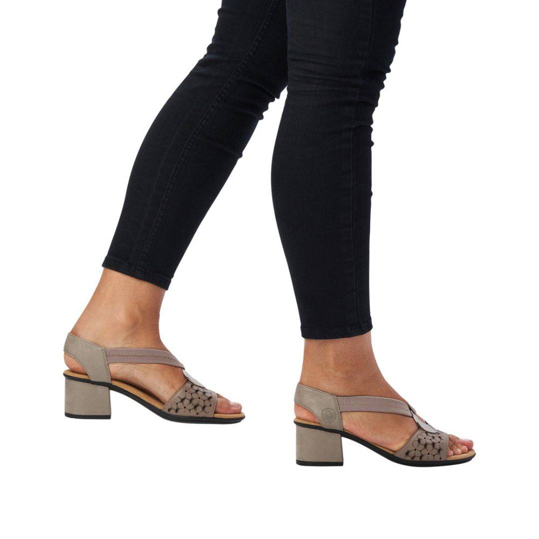 Model wearing taupe Women's Rieker 64677 Sling-Back Heeled Leather Sandal styled with black jeans, showcasing comfort and elegance.