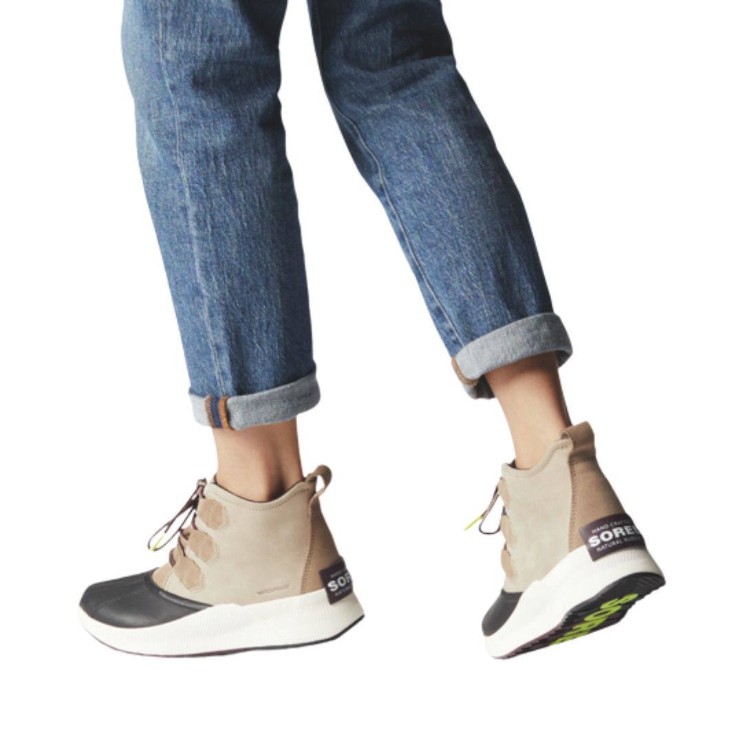 Legs in cuffed jeans wearing taupe suede leather ankle boot with laces and black rubber outsole.