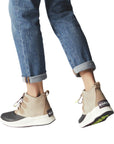 Legs in cuffed jeans wearing taupe suede leather ankle boot with laces and black rubber outsole.