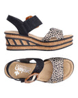 Pair of Black and leopard print straped wedge sandal with a faux buckle on top Velcro strap, tan Rieker logo'd footbed and a faux cork wedge midsole with black accent lines.
