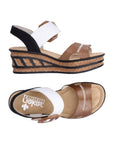 Pair of wedge sandals with Black, white and brown straps, a faux buckle on top Velcro strap, tan Rieker logo'd footbed and a faux cork wedge midsole with black accent lines.