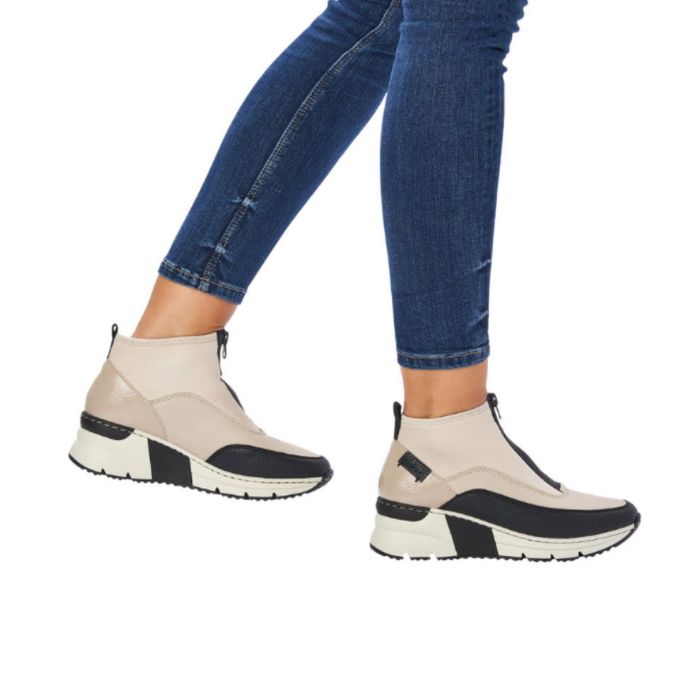Woman in blue jeans wearing a white Rieker top zipper sneaker with black accents and black and white wedge outsole.