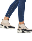 Woman in blue jeans wearing a white Rieker top zipper sneaker with black accents and black and white wedge outsole.