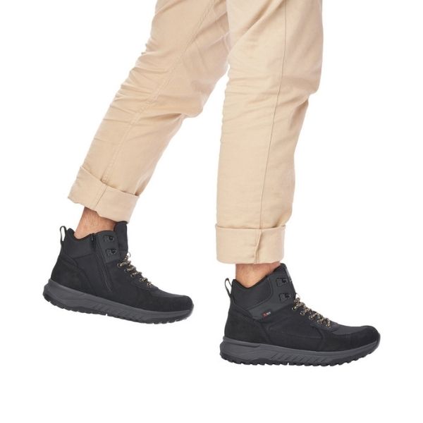 Man in beige pants wearing Rieker&#39;s black winter lace-up ankle boot.