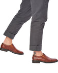 Model wearing brown Rieker 17659 leather dress shoes with rolled-up pants. Stylish slip-on shoes ideal for casual or dressy looks.