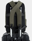 Green backpack with thick shoulder straps sitting on a black suitecase.