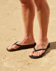 Man wearing black thong sandals on beach.