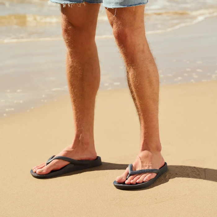 Man wearing grey thong sandals on beach.