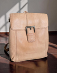 Beige leather backpack on a wooden surface with a neutral background