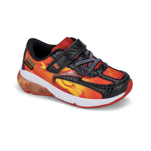 A toddler's athletic sneaker featuring a red, orange, and yellow flame pattern on a black base, with a hook-and-loop strap closure and a white midsole.
