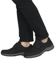 Legs in black pants wearing black shoe with Velcro closure and grey midsole.