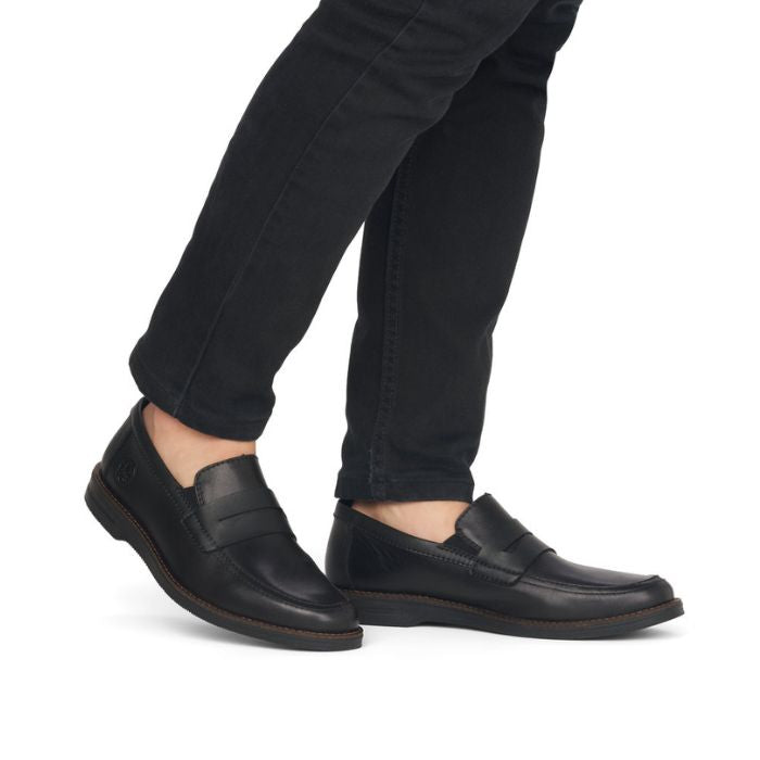 Men in in black jeans wearing black leather penny loafer dress shoe.