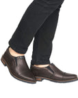 Men in black jeans wearing brown leather slip-on dress shoe with toe cap and navy accents and navy outsole.