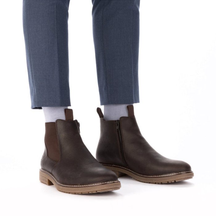 Brown leather chelsea boots worn with dusty blue dress pants and white socks.