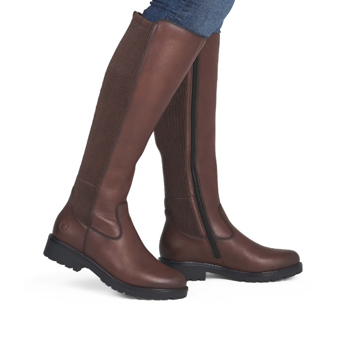 A pair of knee-high brown leather riding boots with ribbed knit shafts worn with blue jeans.