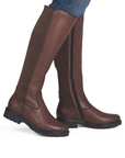 A pair of knee-high brown leather riding boots with ribbed knit shafts worn with blue jeans.